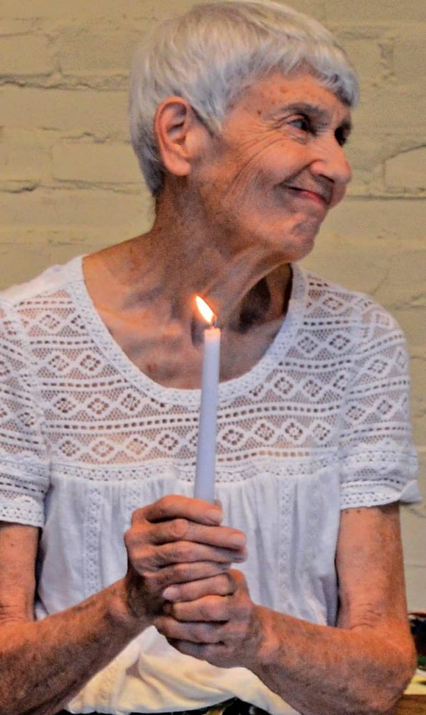 An older woman with short gray hair holds a candle and smiles