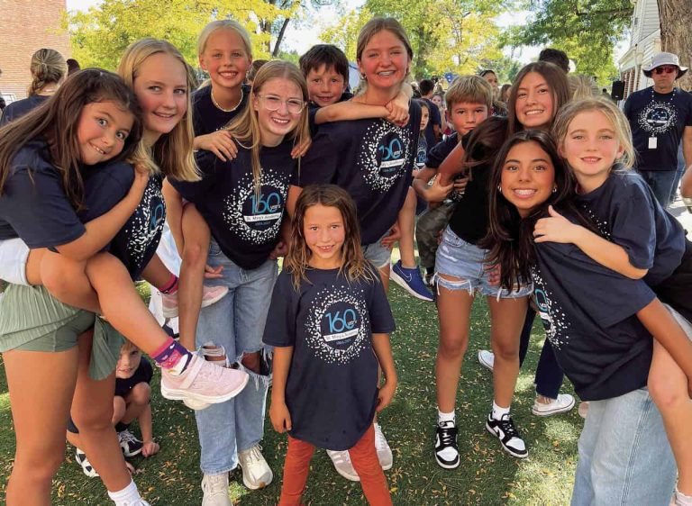 Smiling elementary and high school students gather together outdoors in summer