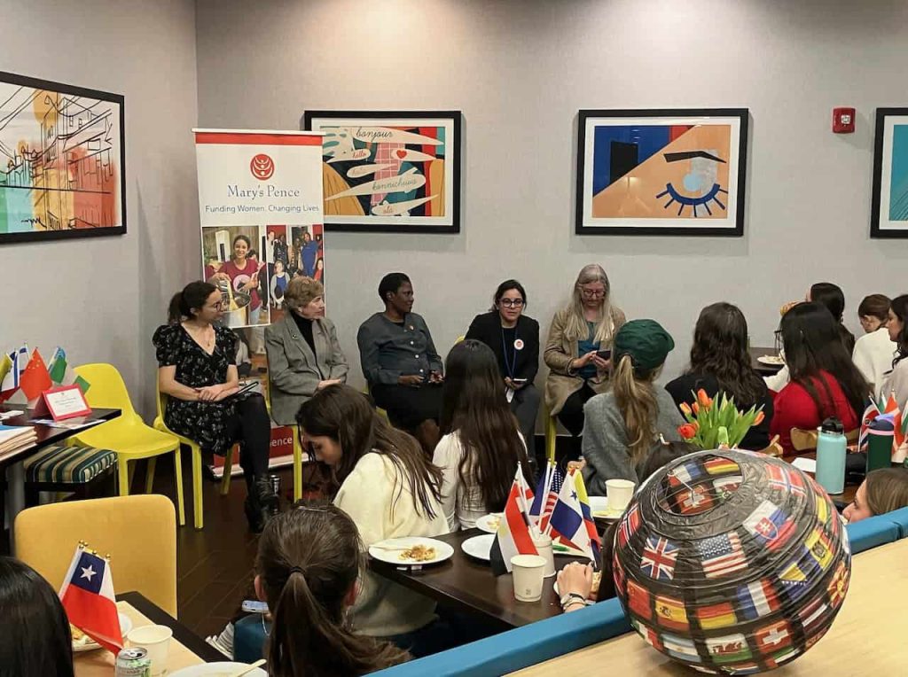Five women on a panel in a room filled with colorful art are engaging with a group of young people intently listening.