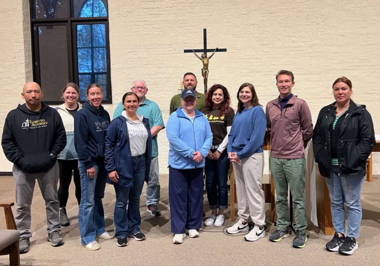 A group of several teachers on a retreat in a chapel standing and smiling together.