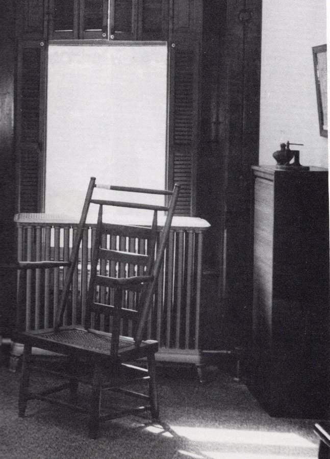 Archival black and white photo of an office space with a wooden chair and large window.