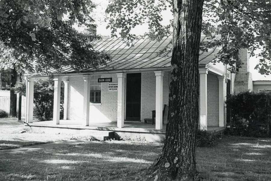 Black and white archival photo of a white brick house surrounded by trees. A sign hanging from the front porch reads "Badin Lodge."