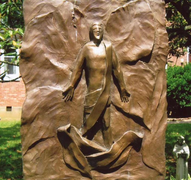 A sculpture of the Risen Christ emerging from a textured, bronze background.