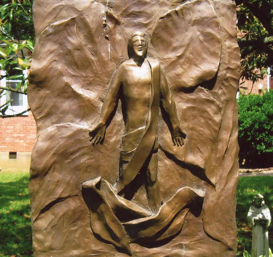 A sculpture of the Risen Christ emerging from a textured, bronze background.