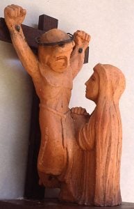 A statue Station of the Cross 12 - Jesus dies on the cross. Jesus is shown on the cross as a woman prays before him.