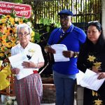 An older white woman, an older Black man and a middle aged Vietnamese woman are pictured attending a memorial service for victims of a plane crash.