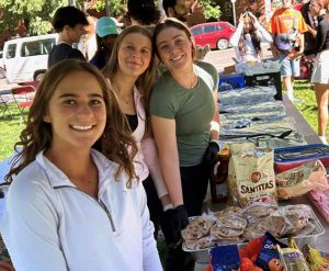 Three high school students smiling outside as they work at a lunch and clothing drive in their city.