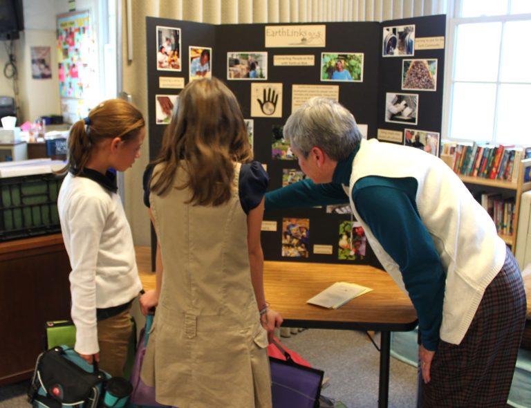 A woman points out something on a table to two students.