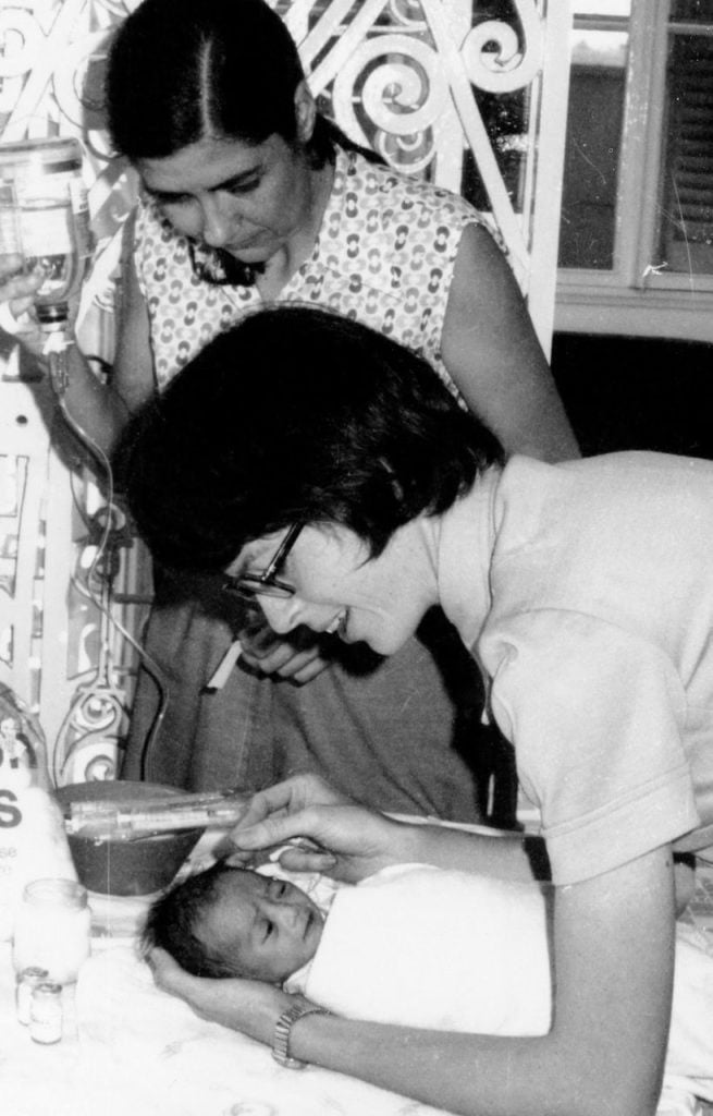 A black and white photo of two women tending to an infant.