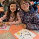 Two elementary students are shown smiling as they color prayer flags for peace.