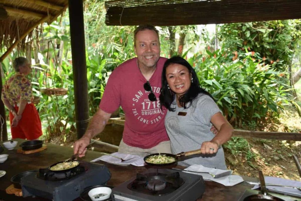 A husband and wife have big smiles as they are frying something in a skillet in an outdoor cooking class.