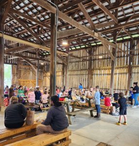 A group of people sitting at wooden tables in a restored wooden barn.