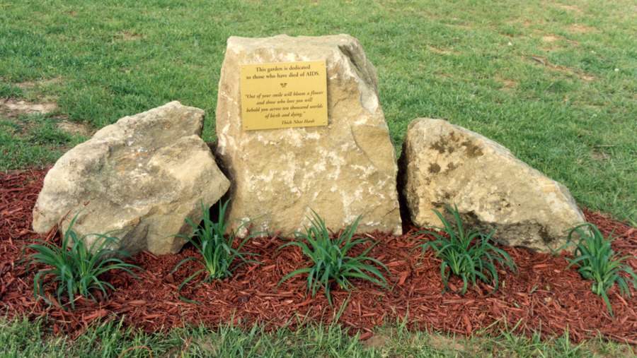 Three large stones arranged together, the center one with a plaque on it. Mulch is around the stones and the decorative grasses in front of them.
