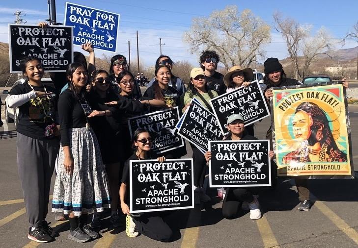 A group of Native American young people pose for a photo holding signs reading "