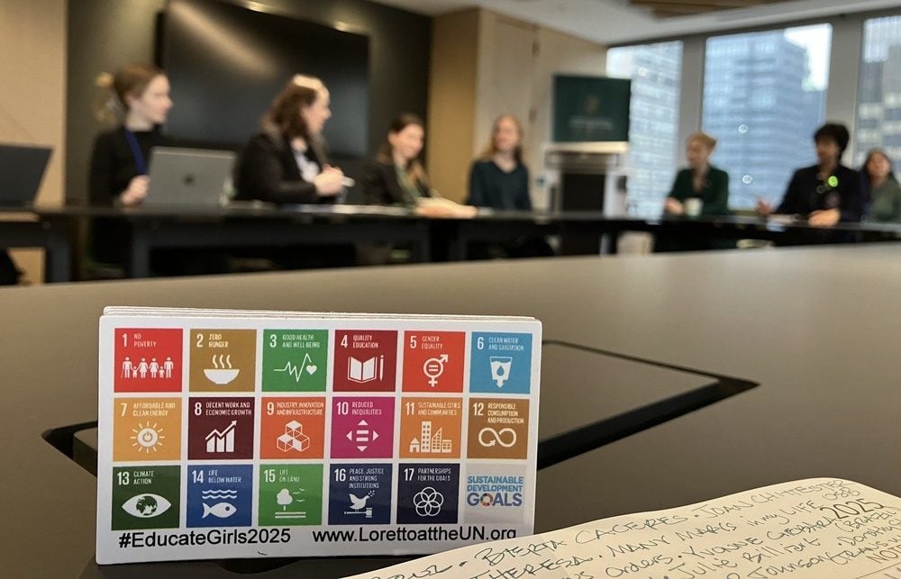 A small display card with colorful grid-like symbols placed on a large meeting table with a page of notes in the bottom right corner pictured during an active discussion.
