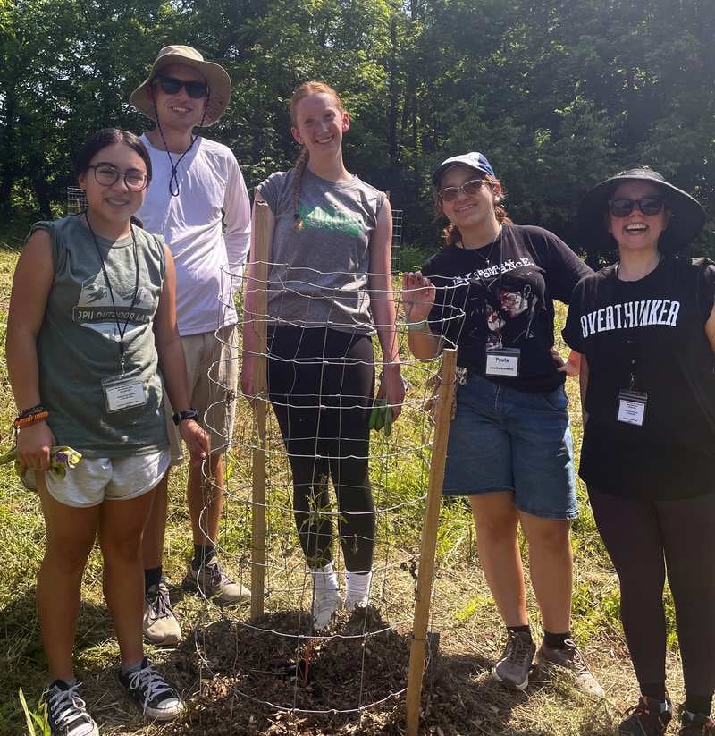 5 volunteers smile around a newly installed cage around a small tree on a sunny day.