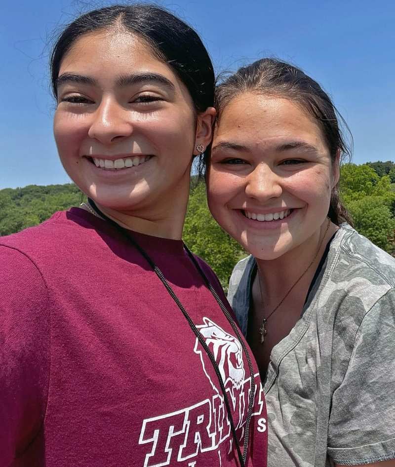 Two young girls smile together for a selfie outdoors on a sunny day.