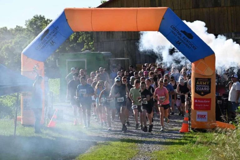 A group of runners at the start of a 5k. Smoke billows around them to signal the start of the race.