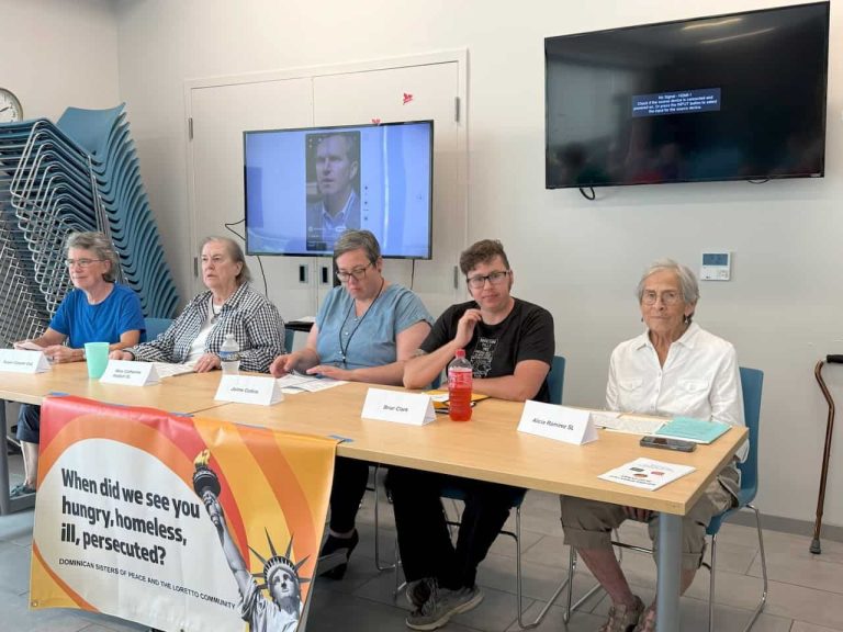 A group of five people sitting at a table at the front of a room on a panel.