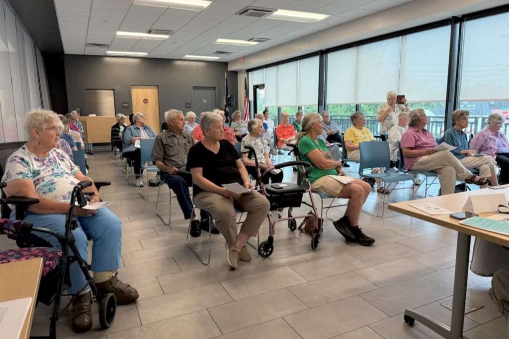 A group of elders, some religious community members, at a speak out event in a bright room in a library.