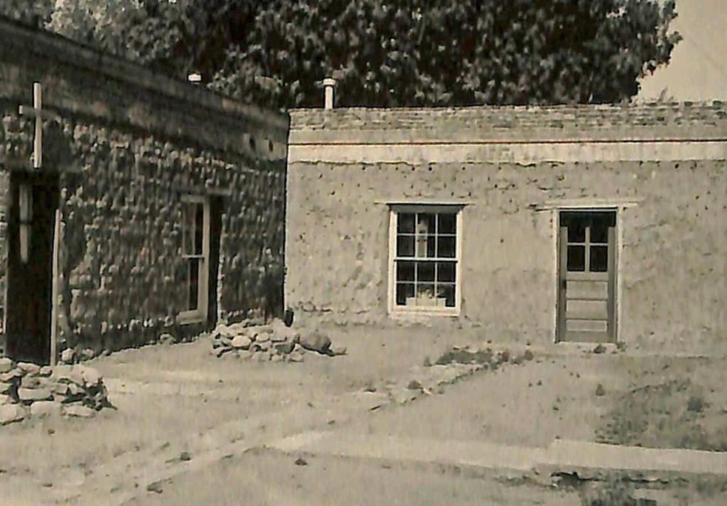A black and white photo of a brick building with a patio area and vegetation in the foreground.