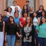 A group of sixteen Latino college students standing staggered on several steps smiling for a group photo.