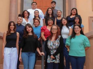 A group of sixteen Latino college students standing staggered on several steps smiling for a group photo.