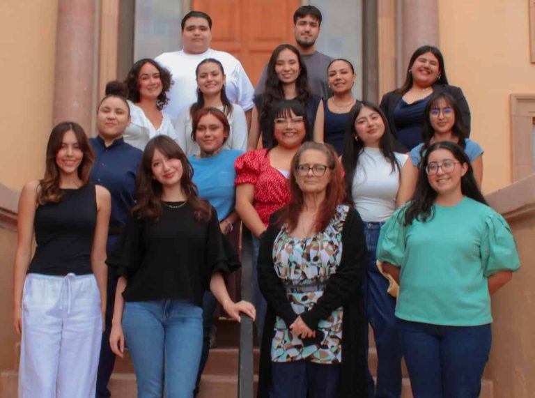 A group of sixteen Latino college students standing staggered on several steps smiling for a group photo.