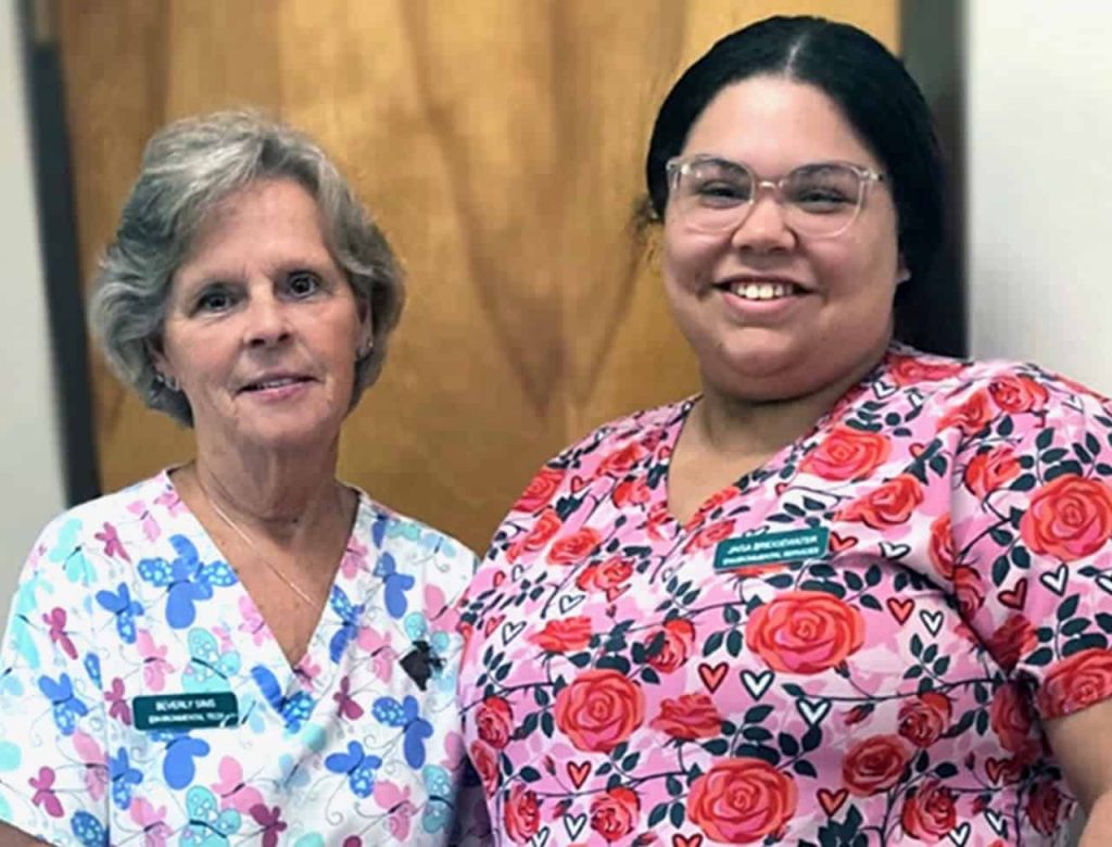Two nurses in bright scrubs smile for a photo together.