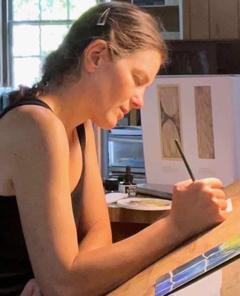 A young white woman with a single braid shown from the side painting.