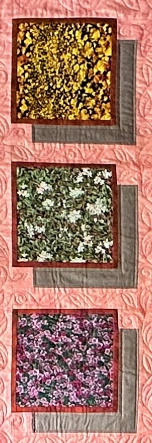 a pink quilt with three rectangle flowery pieces that seem to jump out at you in a 3D quality