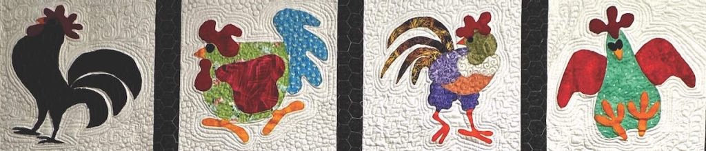 A panel of four roosters in various colors next to one another on a quilt.