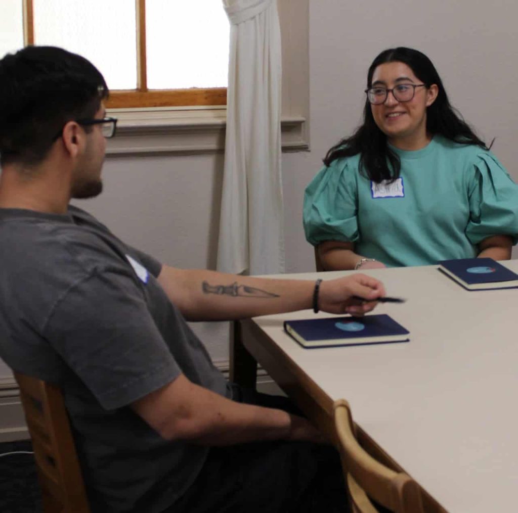 Two young Latino college students engaging in a conversation while sitting at a table.