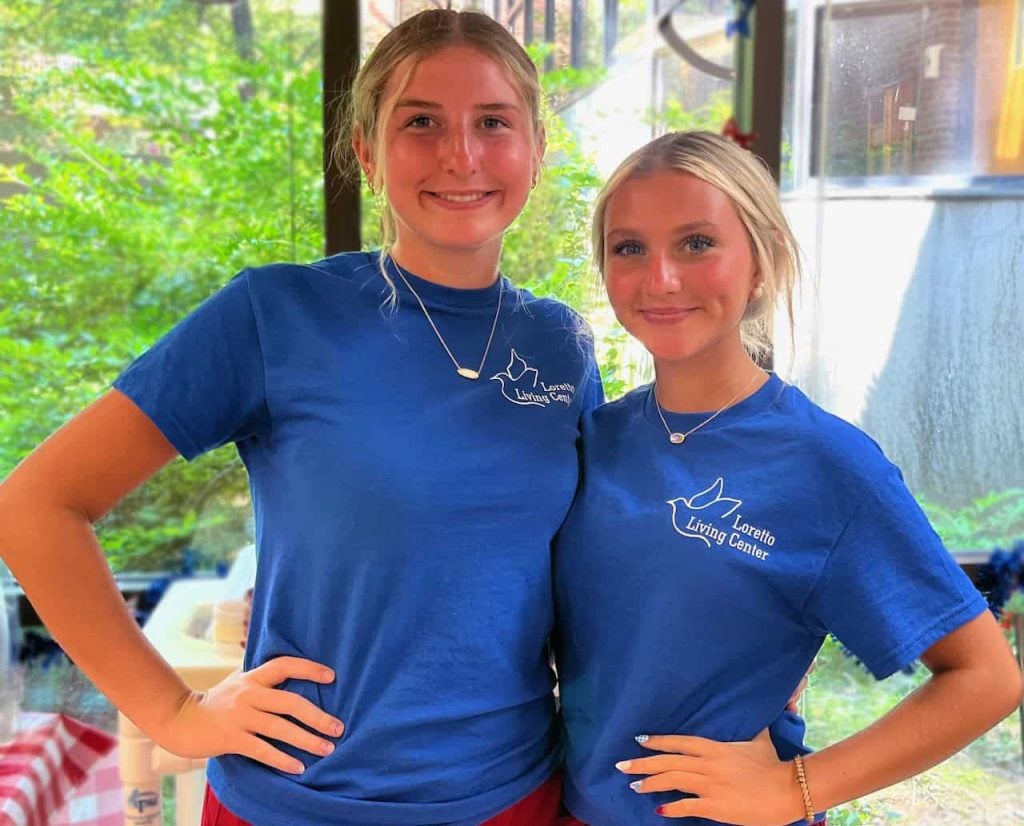 Two young girls smiling together wearing bright blue shirts that say "Loretto Living Center" on them.