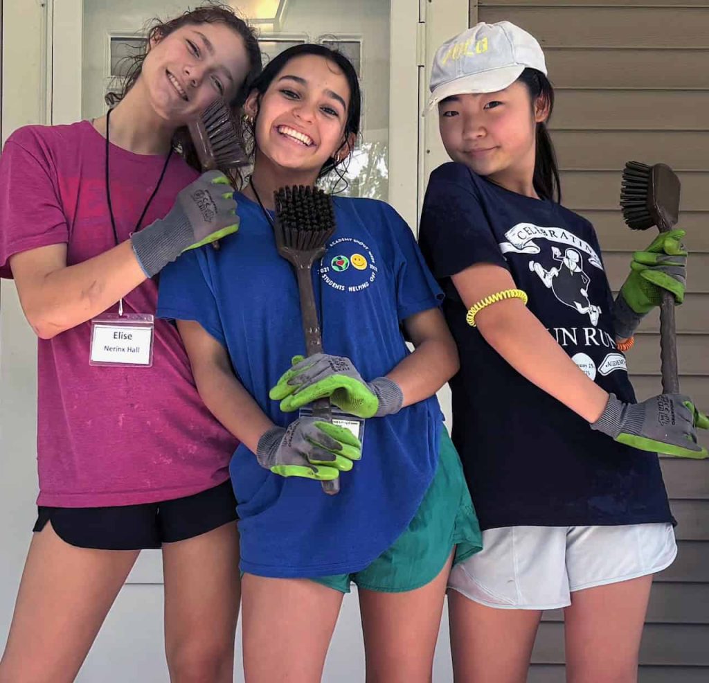 Three high school girls pause for a silly photo while cleaning the porch on one of the Motherhouse homes.