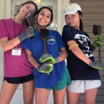 Three high school girls pause for a silly photo while cleaning the porch on one of the Motherhouse homes.
