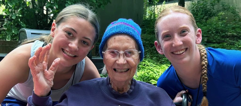 A woman in her 90s, center, enjoys time with high school student volunteers.