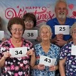 A group of nursing home staff members on valentines day holding up signs with numbers that signify how long they have worked at the Loretto Living Center. The signs range from 25-44 years.