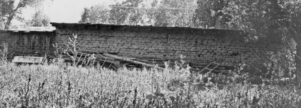 a black and white photo of a brick building outside in a field that's overgrown.