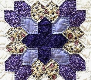 A close up piece of a quilt with a purple and yellow pattern, int he center is a purple cross.