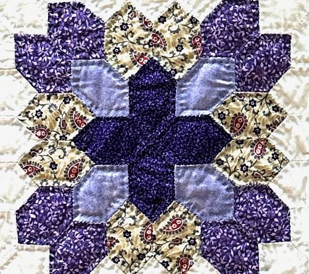 A close up piece of a quilt with a purple and yellow pattern, int he center is a purple cross.