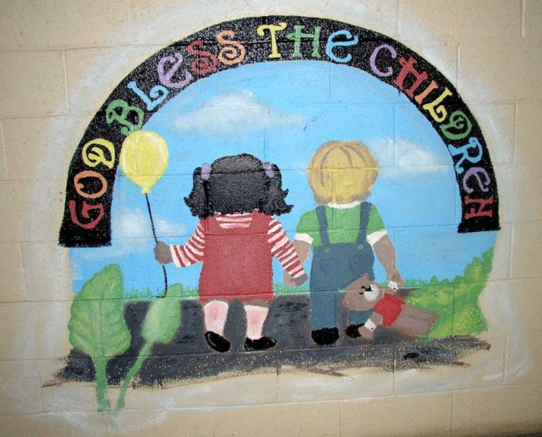 A painted mural of two children holding hands walking on a paved road on a sunny day. Above them is rainbow text that reads "God Bless The Children"