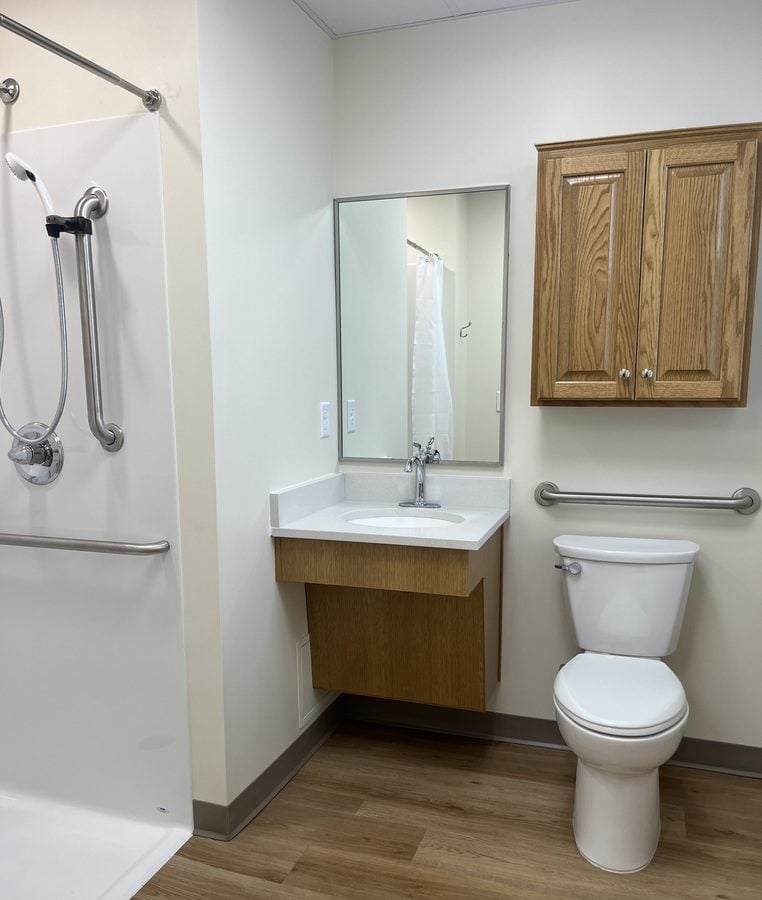 A bathroom with a step-free shower, toilet, sink and cabinet.