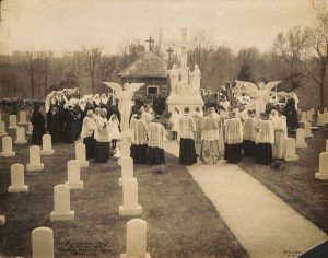 Archival photo of sisters and priests gathered around a statue of the crucifixion in the our Lady of Sorrows cemetery. Handwritten text on the lower left corner of the photo reads "Foundation Day April 25, 1912 Loretto Mother House Kentucky." Royal Photo Lou. Ky