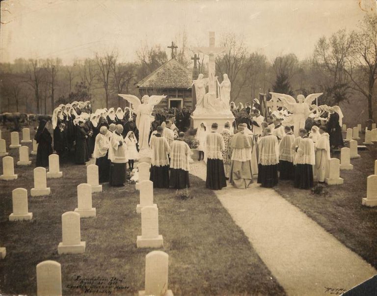 Archival photo of sisters and priests gathered around a statue of the crucifixion in the our Lady of Sorrows cemetery. Handwritten text on the lower left corner of the photo reads "Foundation Day April 25, 1912 Loretto Mother House Kentucky." Royal Photo Lou. Ky