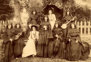 A black and white photo from the 1880s of St. Mary's teachers in full habits and friends enjoying the outdoors. One woman is carrying a banjo and another a guitar.