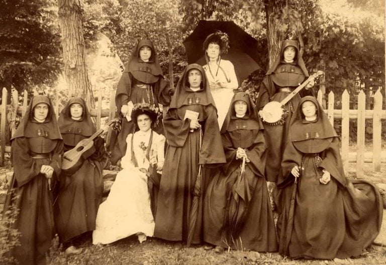 A black and white photo from the 1880s of St. Mary's teachers in full habits and friends enjoying the outdoors. One woman is carrying a banjo and another a guitar.