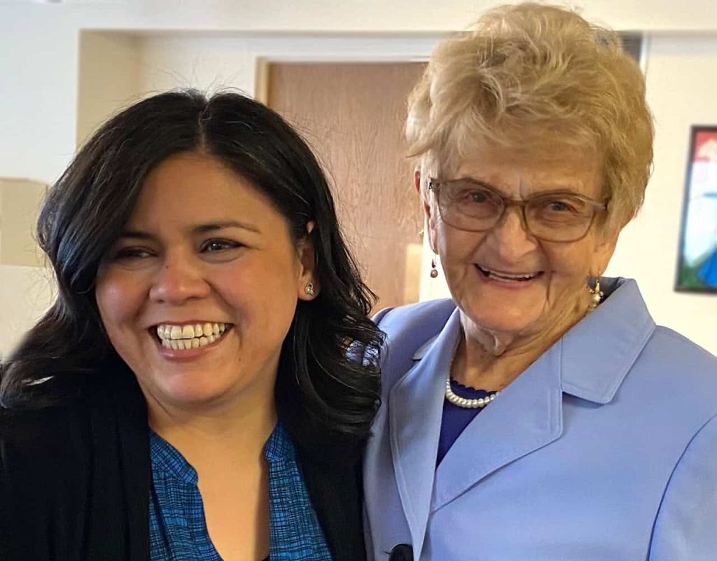 A Latina woman shares a smile with an older white woman at a community event.
