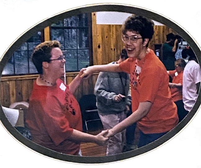 A staff member and resident of a group home dance joyfully together at a community party.