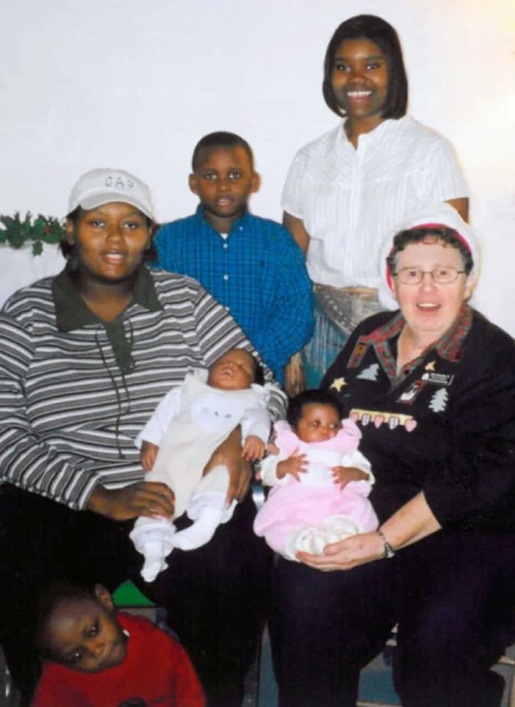 A nun in a Santa hat celebrates Christmas with a family. A mother and her five children.